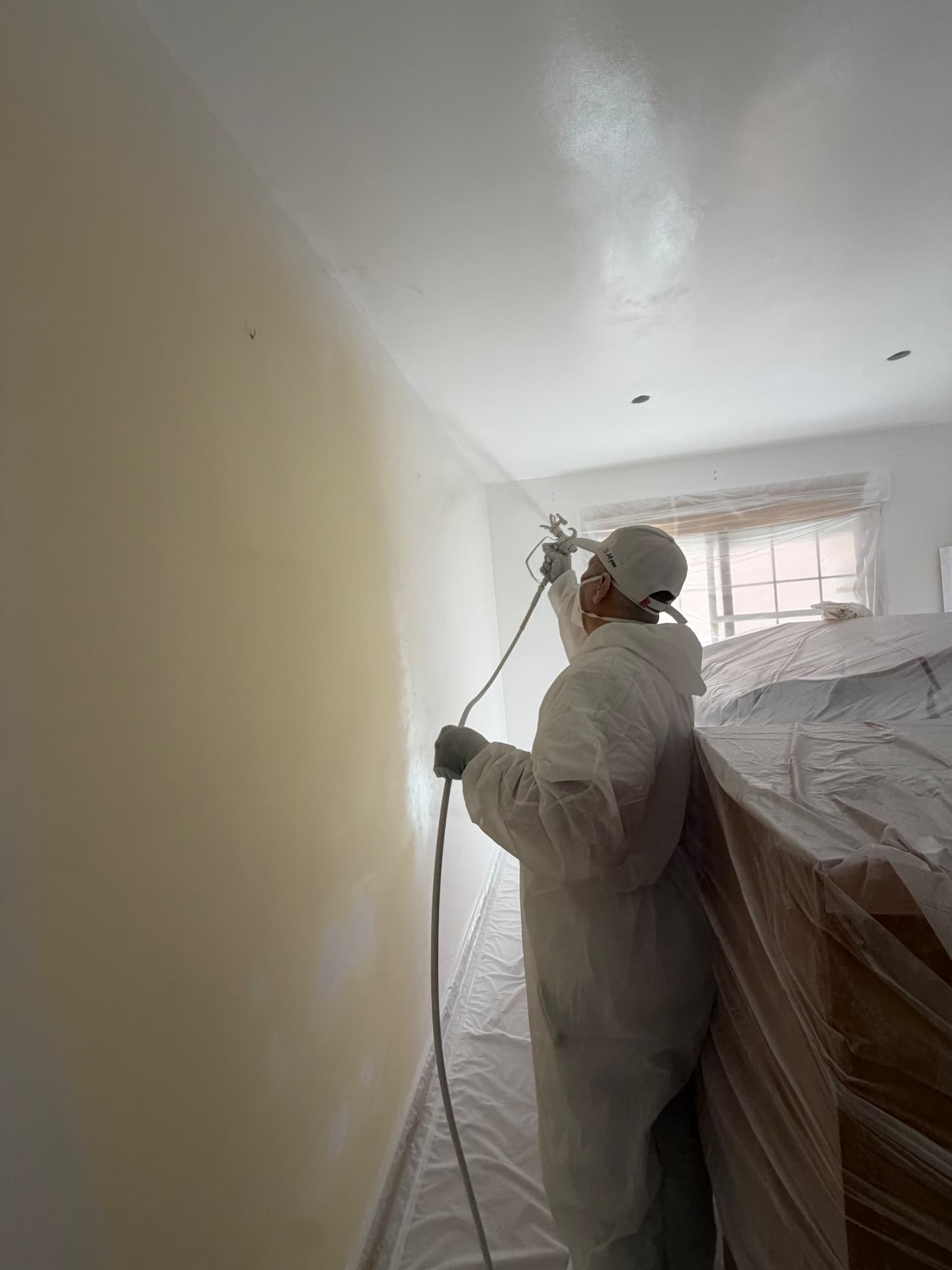 Pintor de ALEMI aplicando pintura con pistola en una habitación protegida